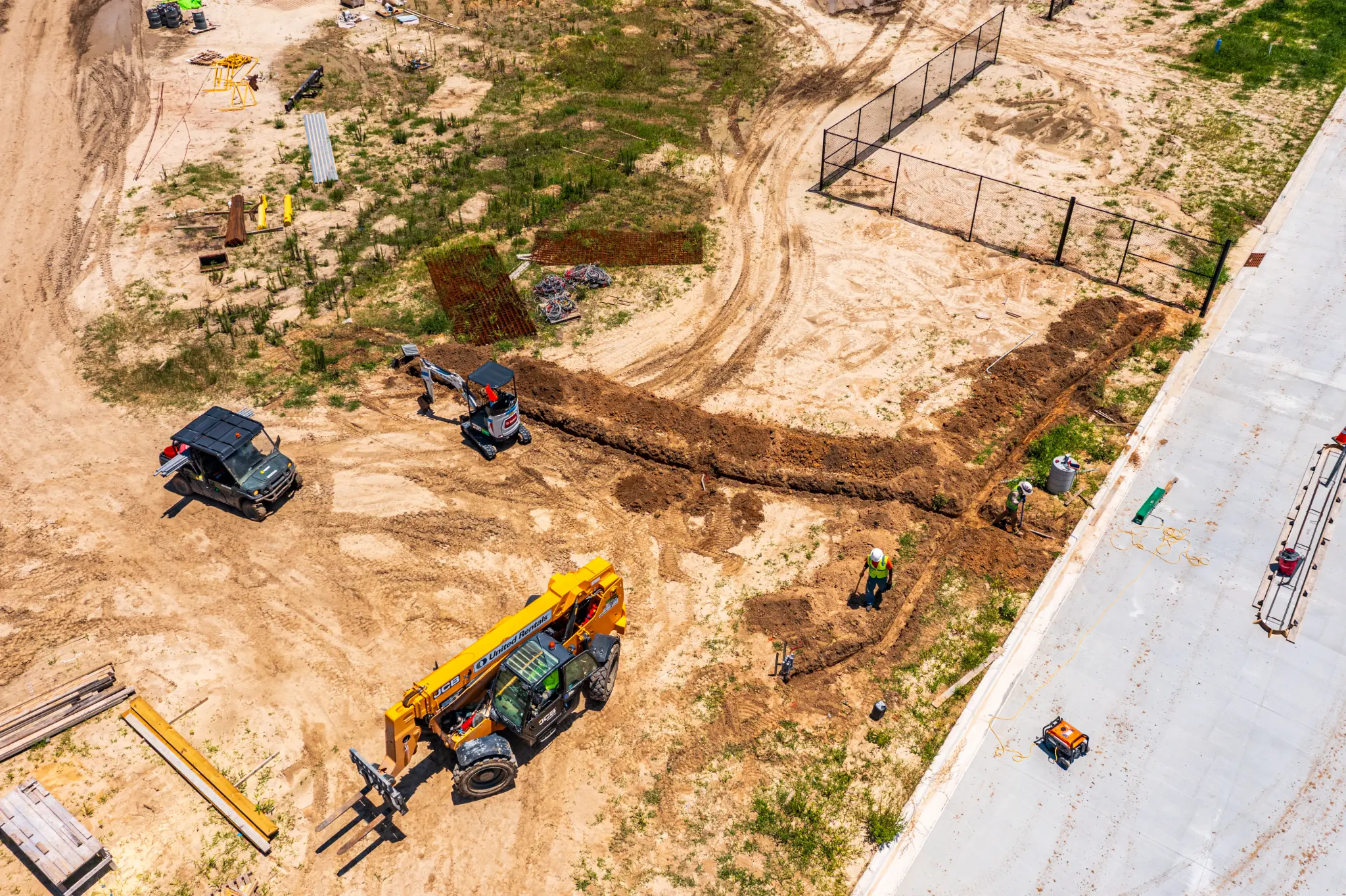 Aerial drone photo of a mini-excavator and JCB telehandler cutting utility trenches beside the Ben E. Keith Foods warehouse, Alachua FL — Visit 66